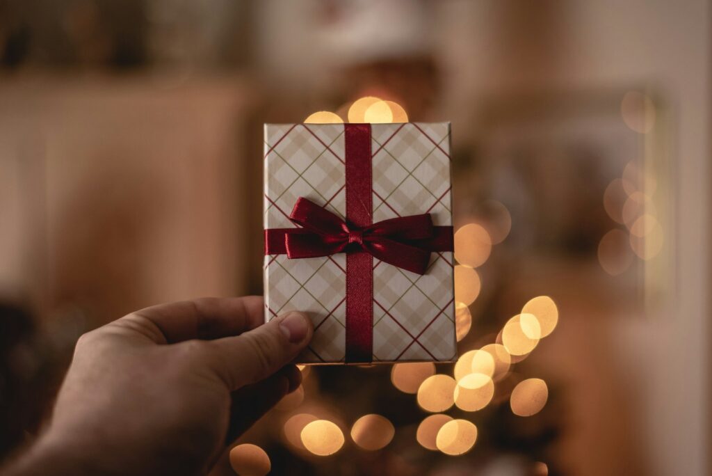 Hand holding a wrapped gift against warm holiday lights